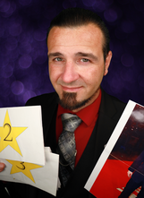 Magician Matthew King headshot in front of purple background and hes holding a magic illusion with numbered yellow stars.