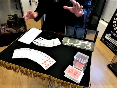 Close-up magician in San Diego seated at table with playing cards, a prop with numbers 1, 2, and 3, and close up magic