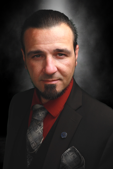 Portrait of San Diego Magician and mentalist Matthew King in black suit with black vest, red shirt, gray tie and pocket square. 
