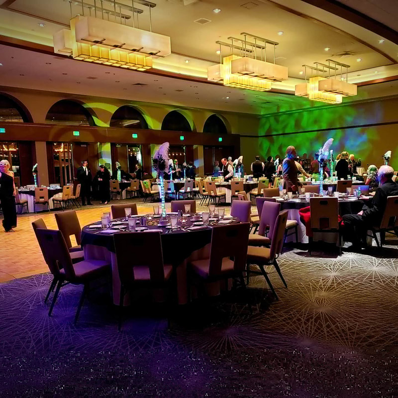 San Diego magician Matthew King performing strolling magic at a corporate event. Image of large room with elegant tables and chairs, and green, purple, and white lighting.